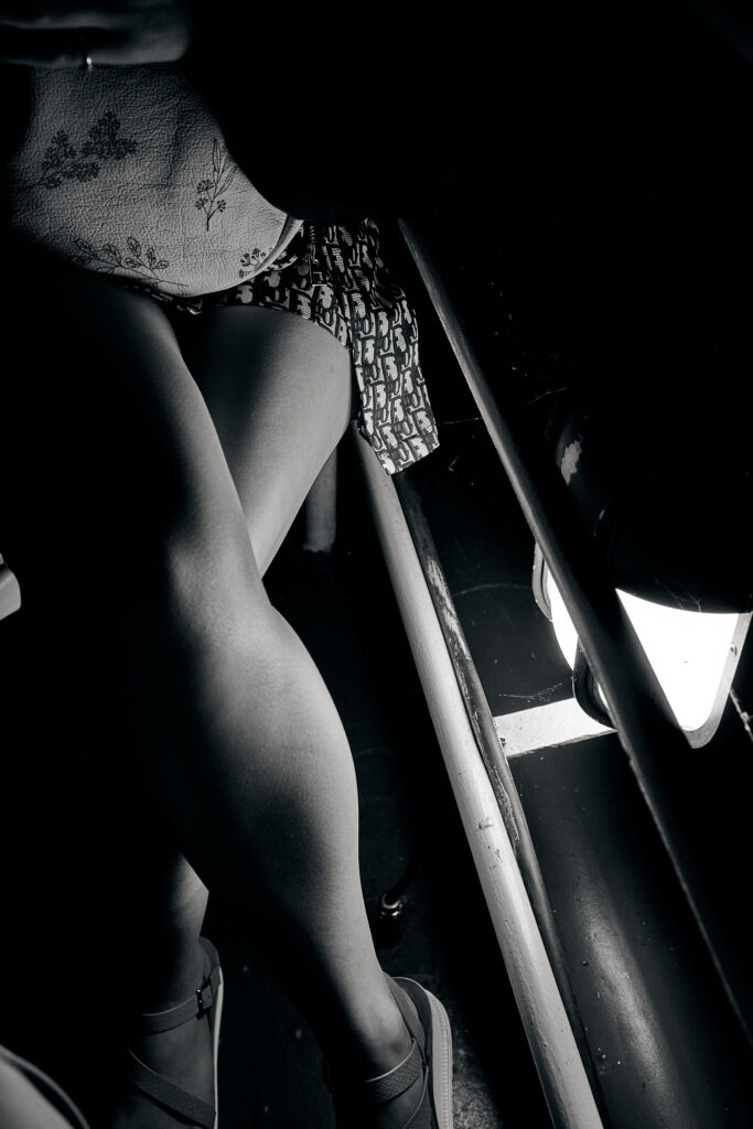 Black-and-white fine art photograph showing the lower half of a seated woman illuminated by dramatic light, captured on traditional film.