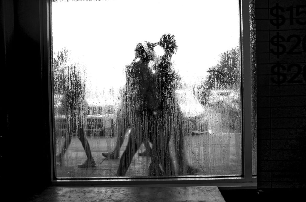 Couple kissing behind a rain-soaked window, with a blurred outdoor scene beyond the glass.